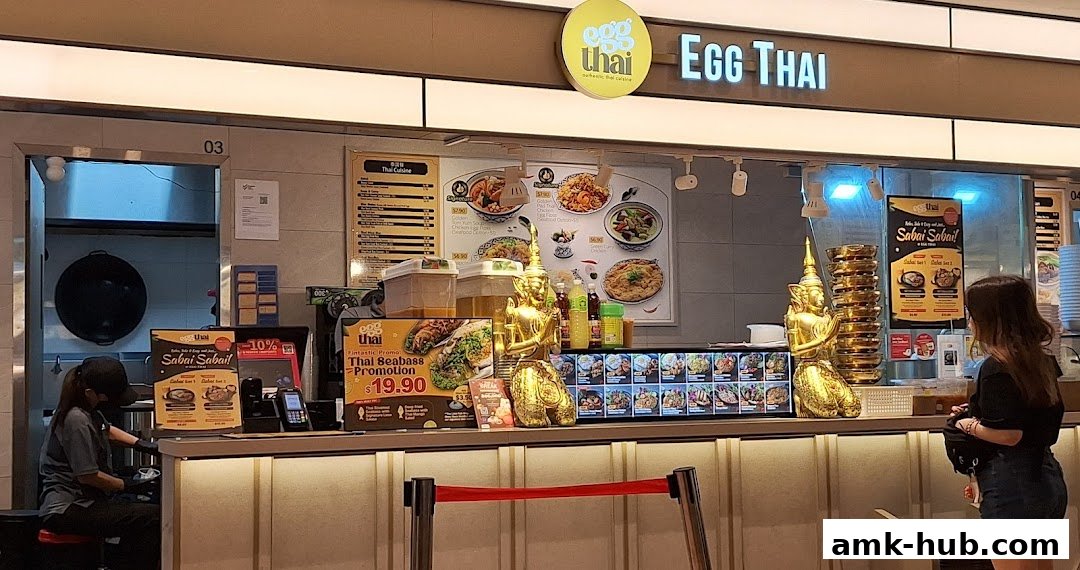 A food stall counter with a menu, food displays, and a customer ordering.