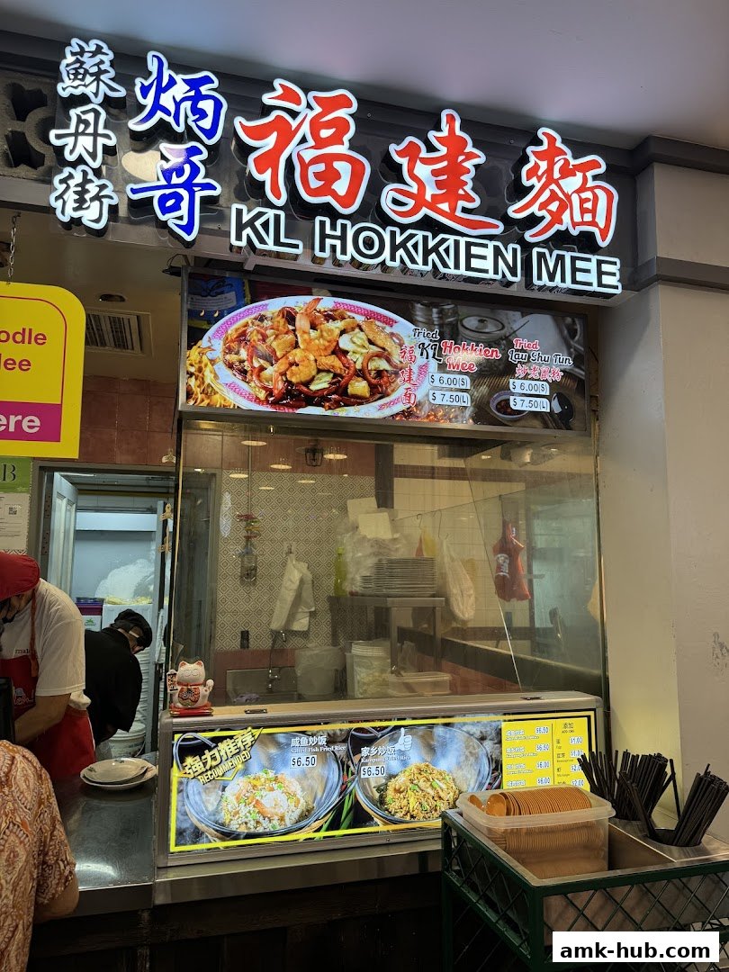 A food stall with a prominent sign for KL Hokkien Mee and images of various dishes.