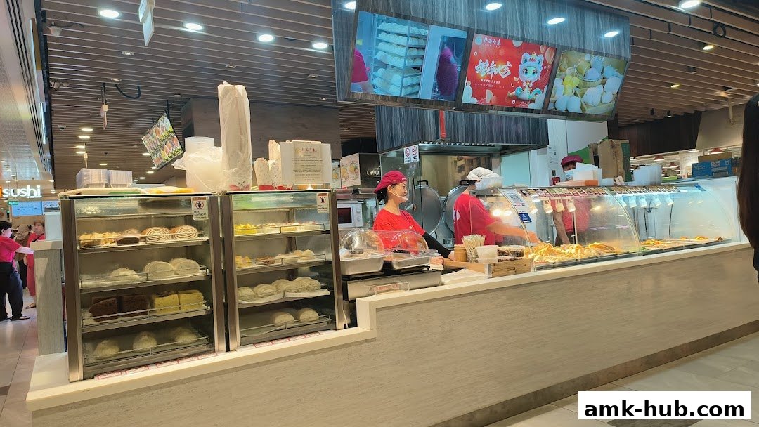 A food stall with display cases filled with pastries and buns, and staff serving customers.