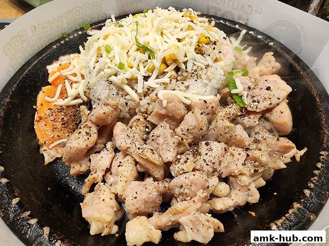 A sizzling hot plate of Pepper Lunch with chicken, salmon, rice, corn, and melted cheese.