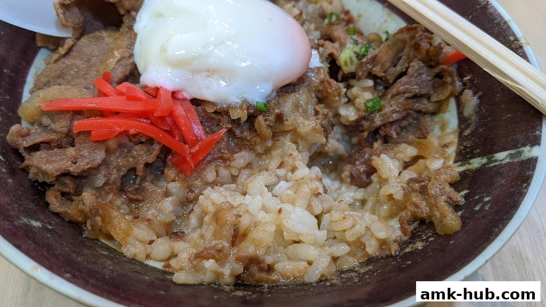 A close-up of a delicious Japanese rice bowl with beef, a soft-boiled egg, and pickled ginger.