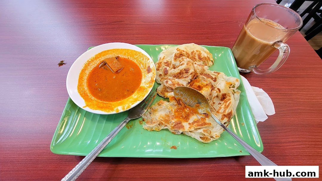 A plate of Roti Canai with curry and a glass of Teh Tarik on a wooden table.