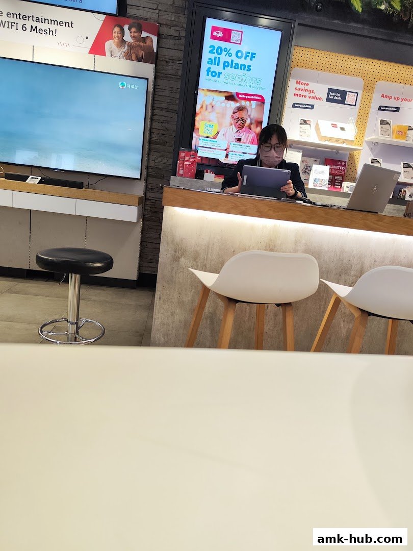 A staff member works at a Singtel shop counter with promotional displays.