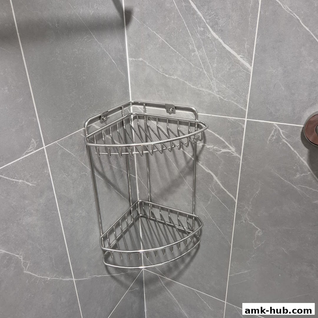 A stainless steel corner shower caddy is mounted on a grey tiled wall.
