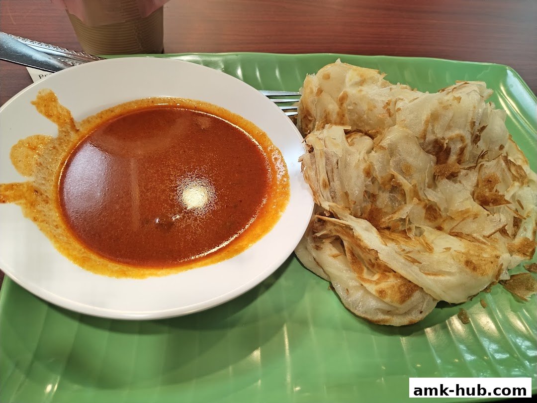 A plate of flaky Roti Canai served with a side of curry sauce.