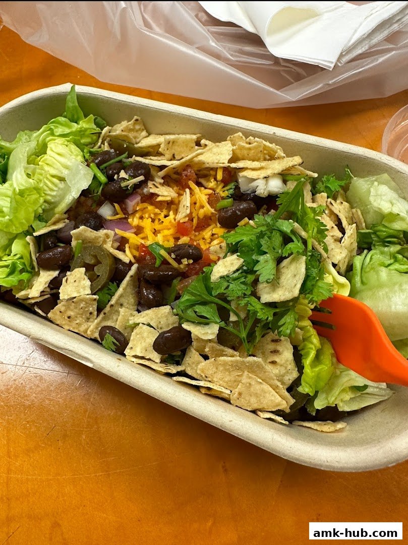 A close-up of a healthy salad with black beans, cheese, salsa, and tortilla chips.