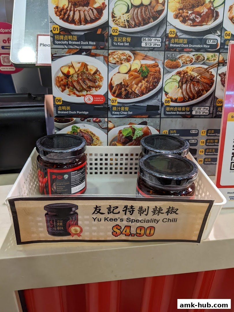 Jars of Yu Kee's Specialty Chili are displayed with a price tag and a menu board in the background.