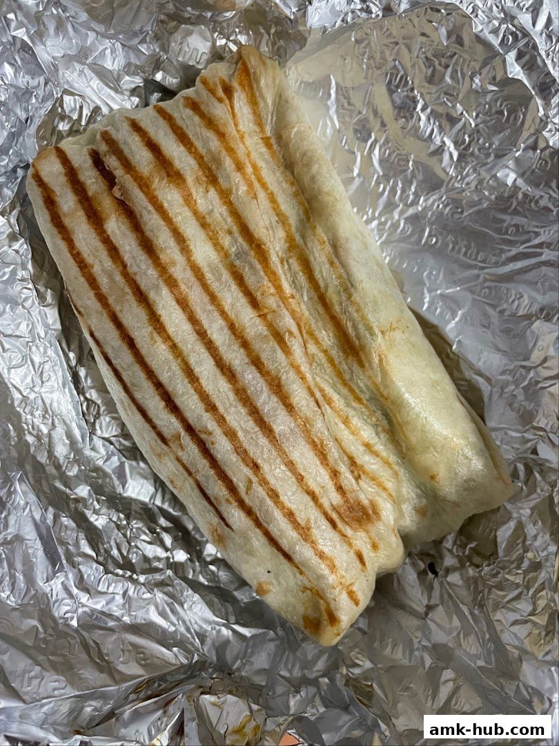 A grilled wrap, likely a burrito or shawarma, is presented on a bed of crumpled aluminum foil.