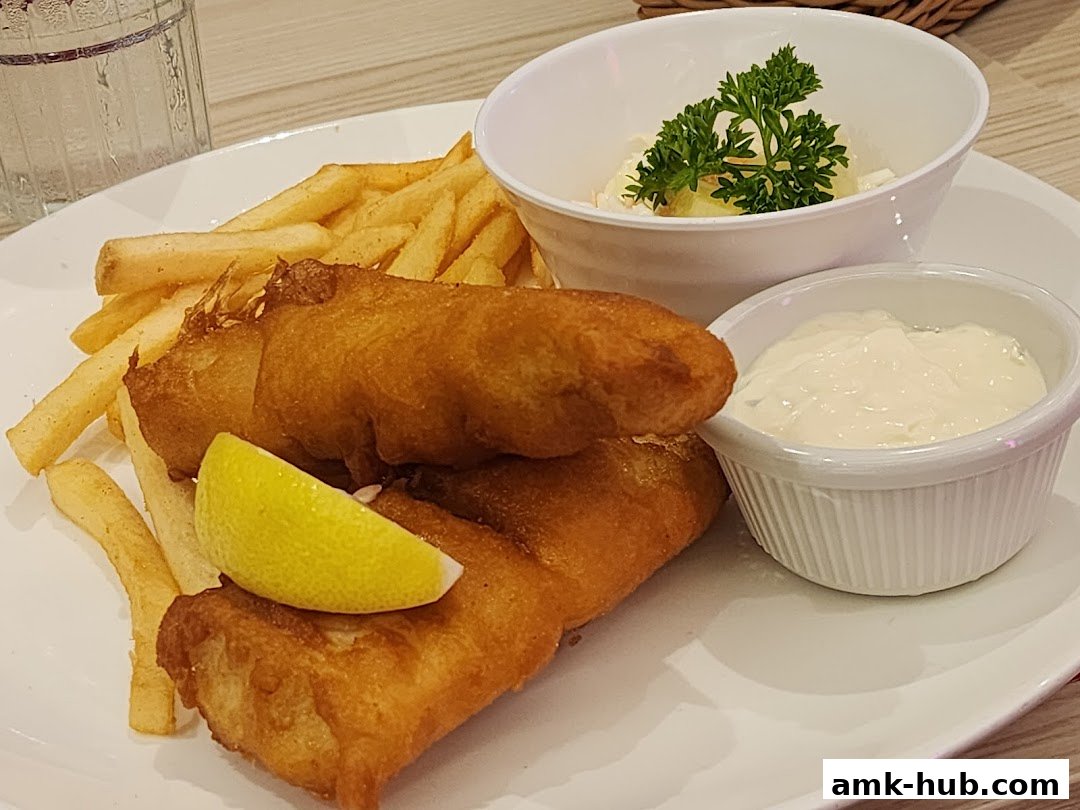 A plate of crispy fish and chips with coleslaw and tartar sauce.