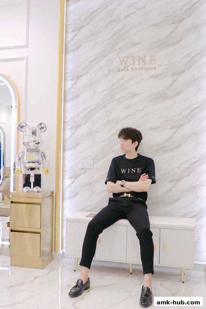 A man sits with arms crossed in front of a marble wall with the Wine Hair Boutique logo.