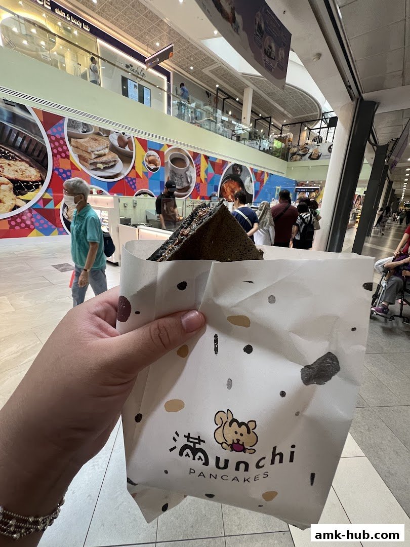 A person holds a paper bag with a pancake from Munchi Pancakes in a mall.