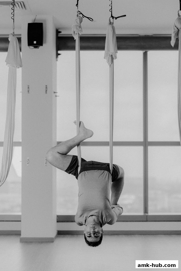 A man is practicing aerial yoga, suspended upside down in a studio.