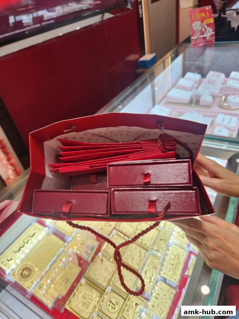 A red shopping bag filled with jewelry boxes and gift cards, with gold bars displayed in a jewelry store.