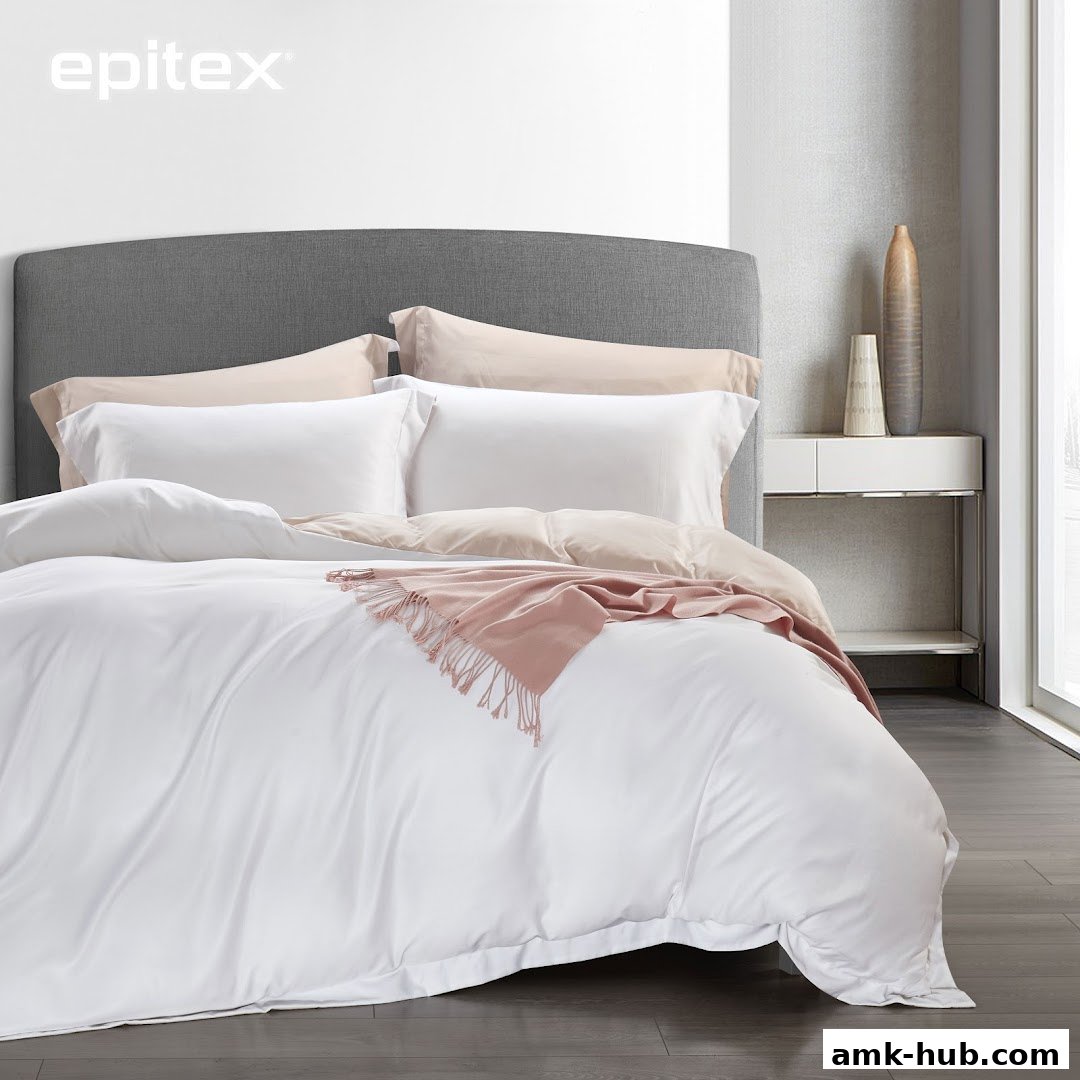 A neatly made bed with white and beige bedding, a grey headboard, and a pink throw blanket.
