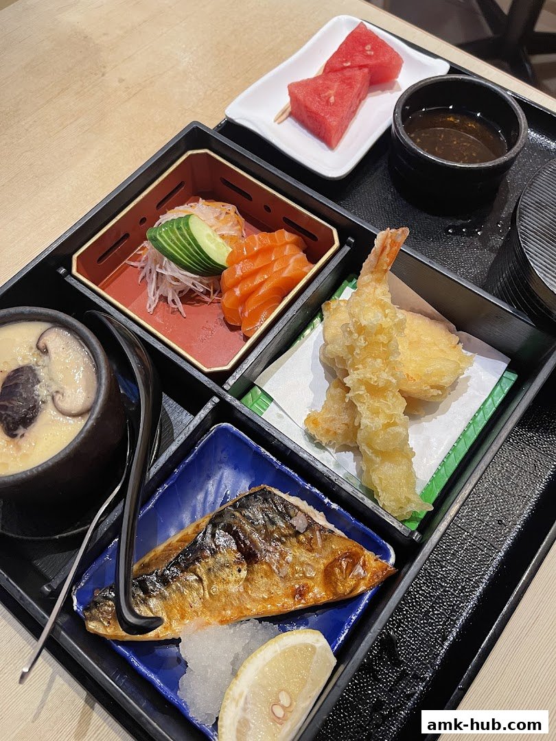A bento box with salmon sashimi, grilled mackerel, tempura, chawanmushi, and watermelon.