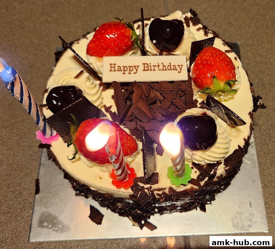 A birthday cake decorated with strawberries, cherries, chocolate shavings, and lit candles.
