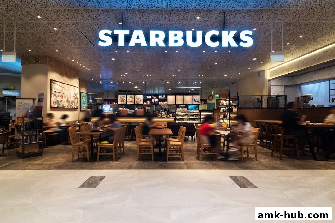 Interior view of a bustling Starbucks cafe with customers seated at tables and the counter visible.