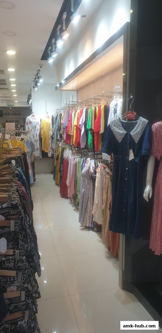 A well-lit clothing store interior with racks of colorful dresses and patterned pants.