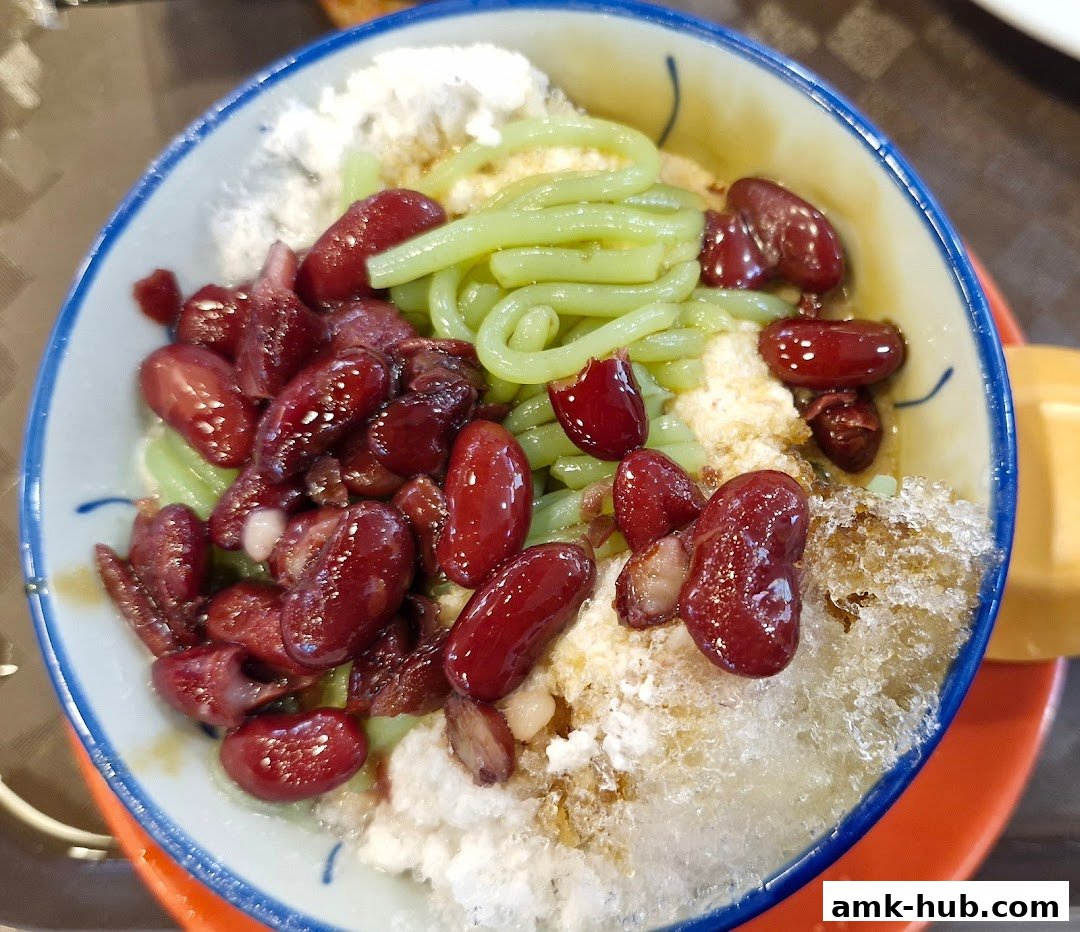 A close-up of a bowl of Cendol dessert with red beans and shaved ice.