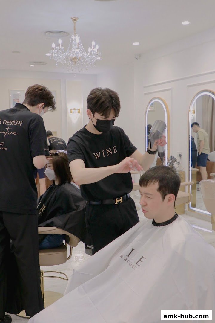 Hair stylists working on clients inside a modern salon with a chandelier.