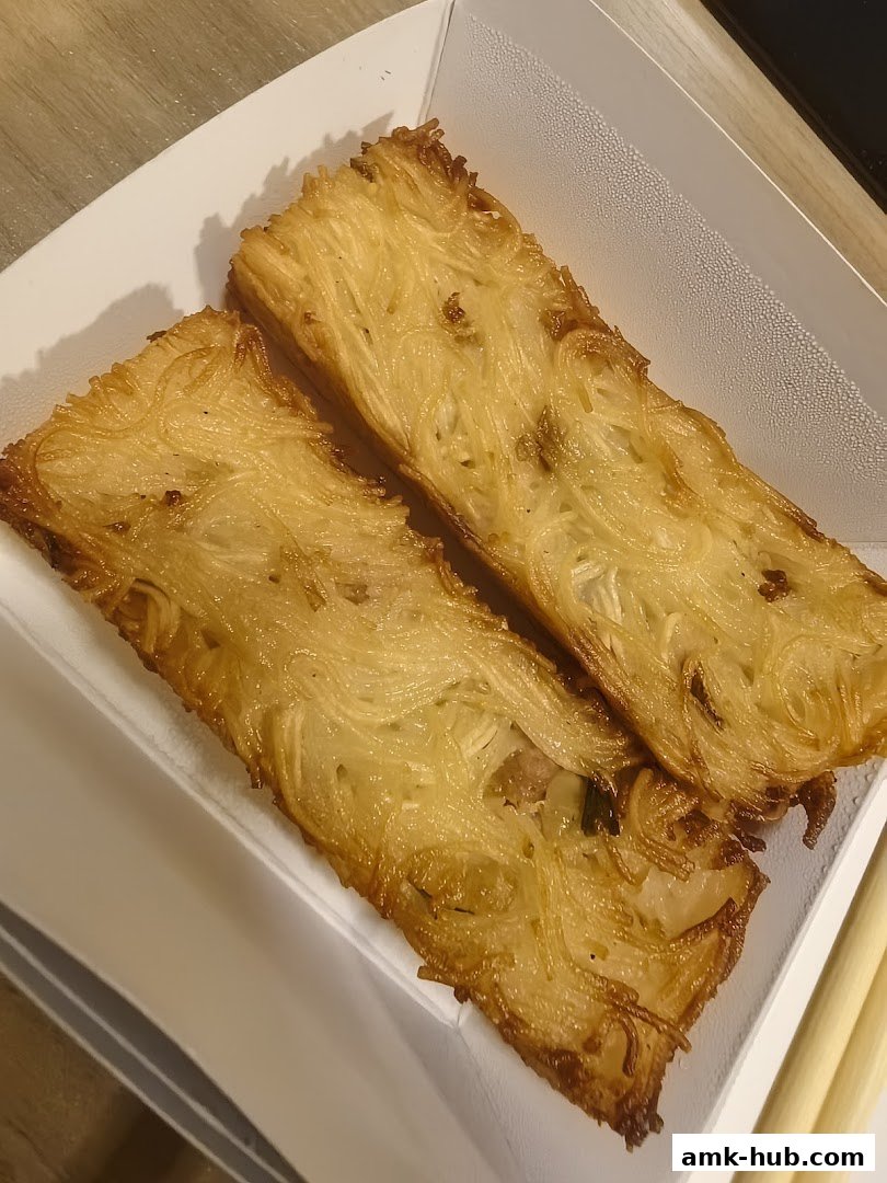 Two golden-brown crispy noodle cakes served in a white container with chopsticks.
