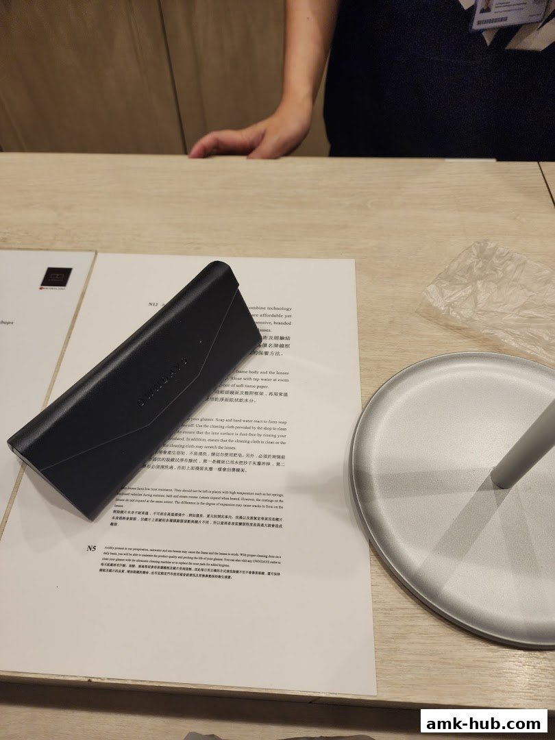 A black OWNDAYS glasses case rests on a document next to a silver stand.