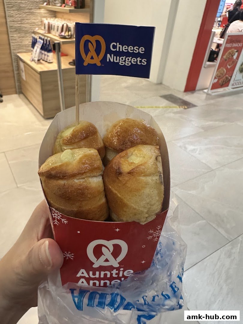 A hand holds a container of Auntie Anne's Cheese Nuggets with a promotional flag.