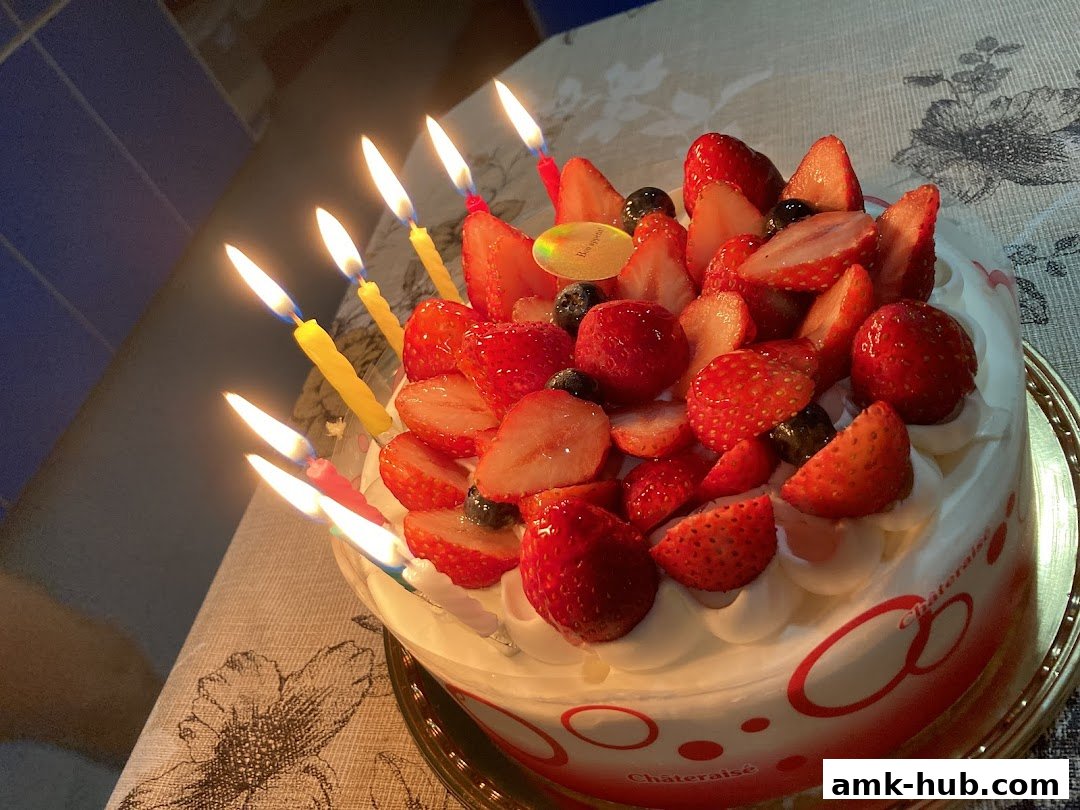 A delicious strawberry cake with lit candles, decorated with fresh strawberries and blueberries.