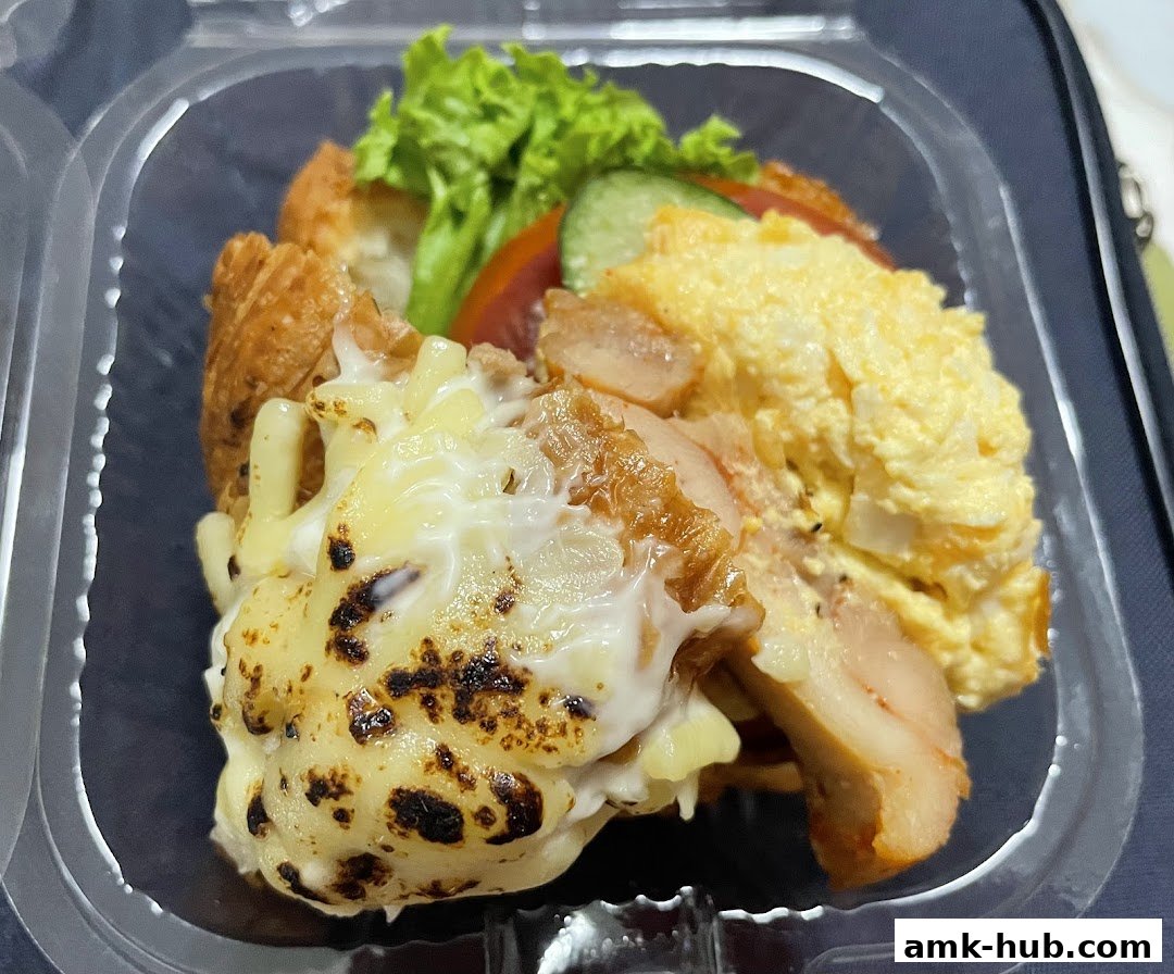 A close-up of a delicious meal in a clear plastic container, featuring cheese-covered pasta, chicken, and scrambled eggs.