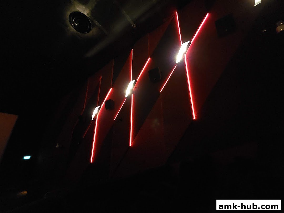 Interior view of a cinema hall with red neon lights and speakers on a red wall.