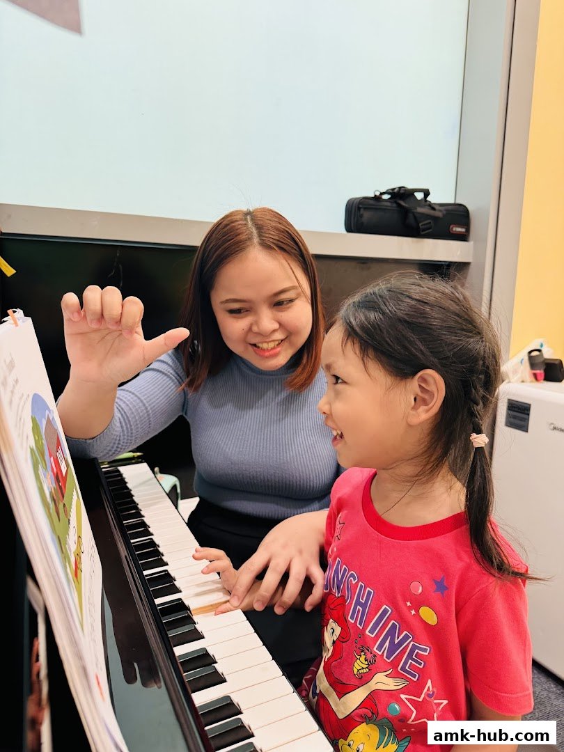 A teacher guides a young student playing the piano, with a music book open.