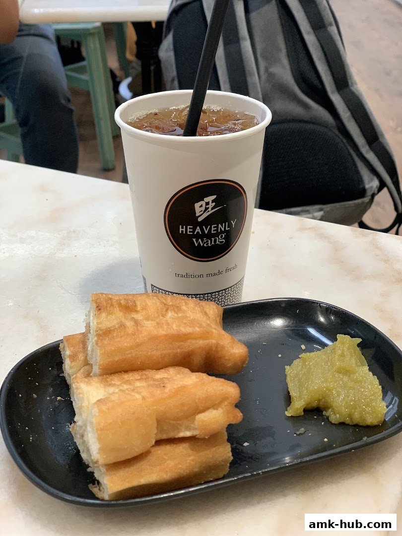 A cup of iced tea and fried dough sticks with a side of green paste on a black plate.