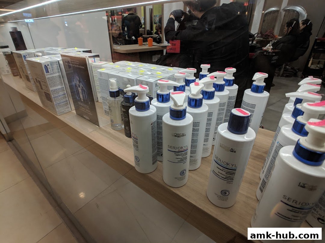 Hair care products displayed on a shelf in a salon with stylists working in the background.
