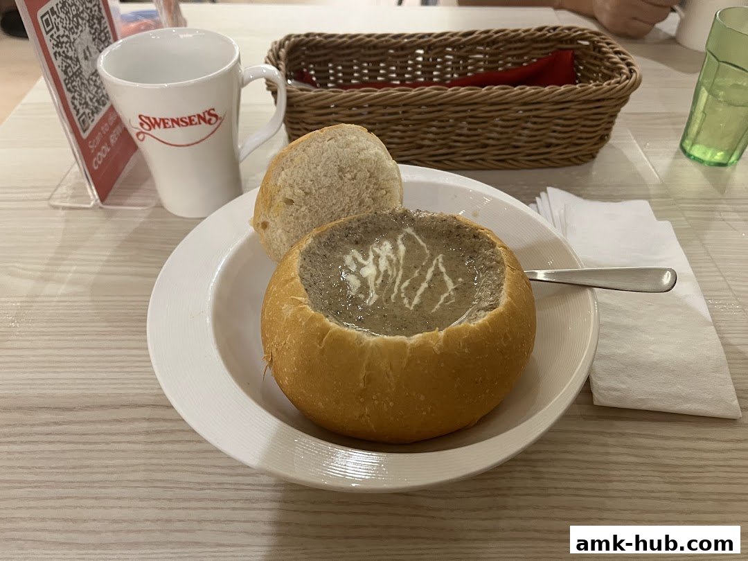A bowl of mushroom soup served in a bread bowl with a side of bread.