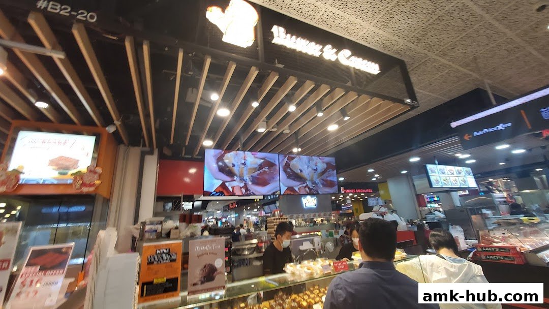 Interior view of a bakery with a display of pastries and a digital menu showing desserts.