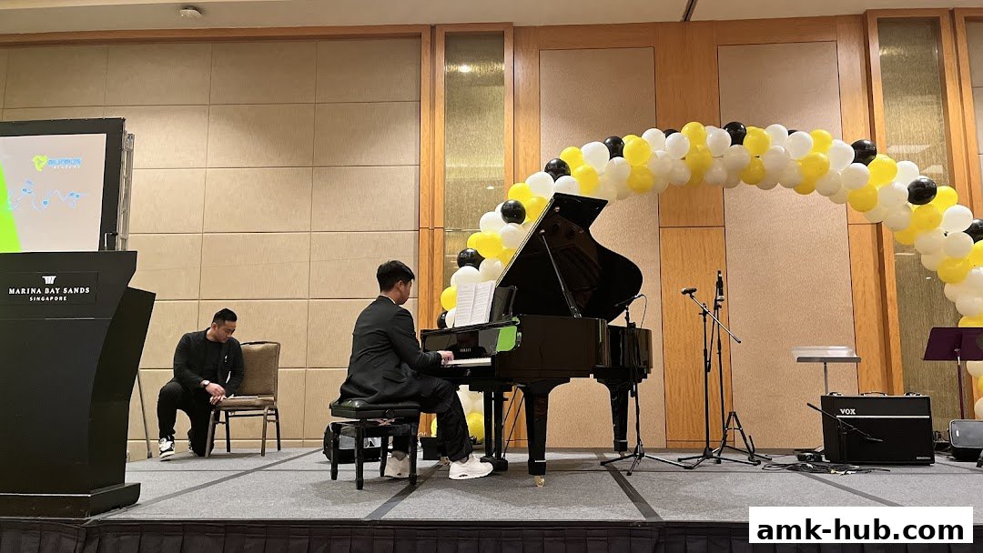 A pianist performs at a grand piano on a stage decorated with a balloon arch.
