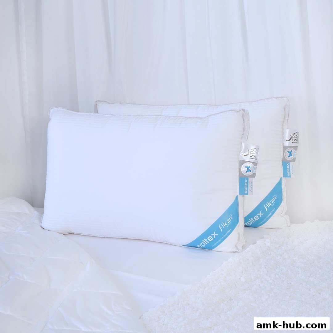 Two white Epitex Filcare pillows are displayed on a white bed with a white sheer curtain in the background.