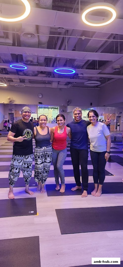 A group of five people smiling and posing for a photo in a yoga studio.
