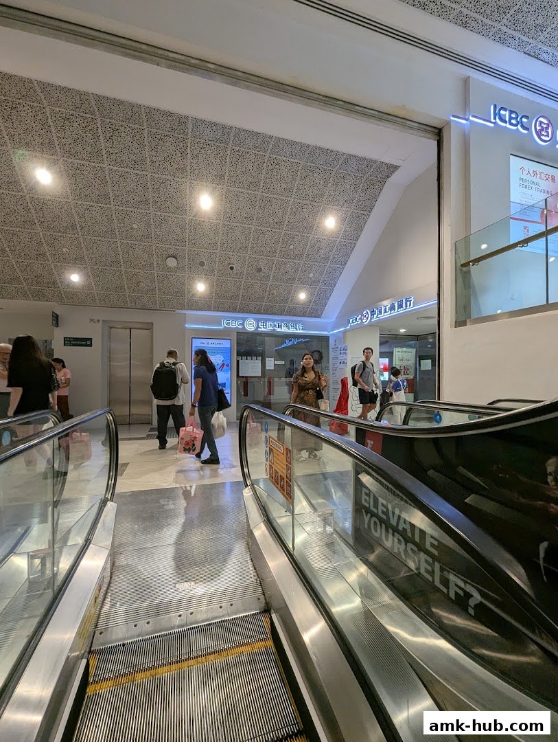 The entrance to ICBC Ang Mo Kio Sub-Branch with escalators and people.