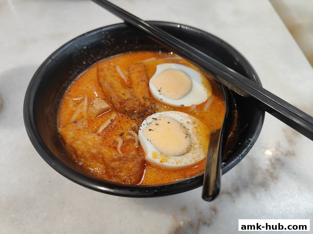 A close-up shot of a delicious bowl of Laksa with half-boiled eggs and chopsticks.