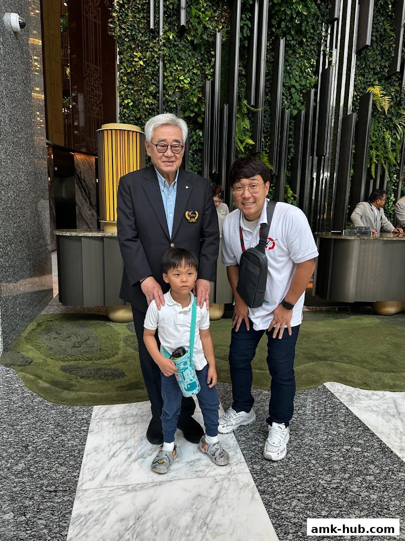 Three people, an older man, a younger man, and a child, pose for a photo in a modern lobby.