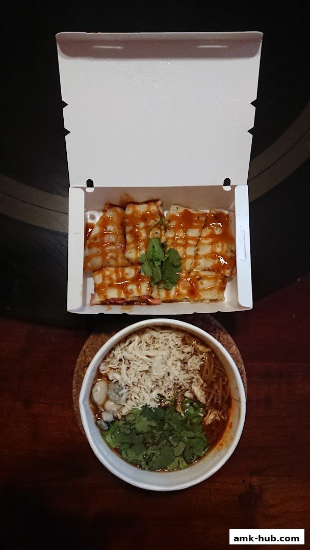 A takeout box filled with Taiwanese snacks and a bowl of noodles with toppings.