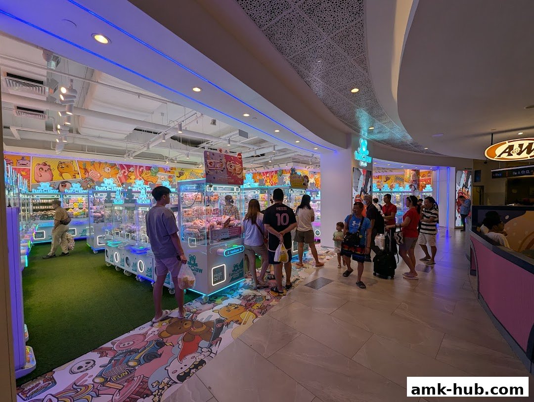 People playing claw machines filled with plush toys in a brightly lit arcade.