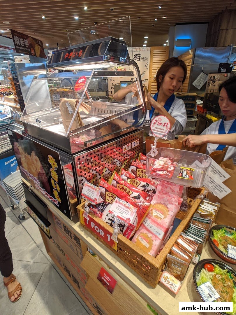 Staff members at Kuriya Japanese Market arranging snacks and prepared food items.