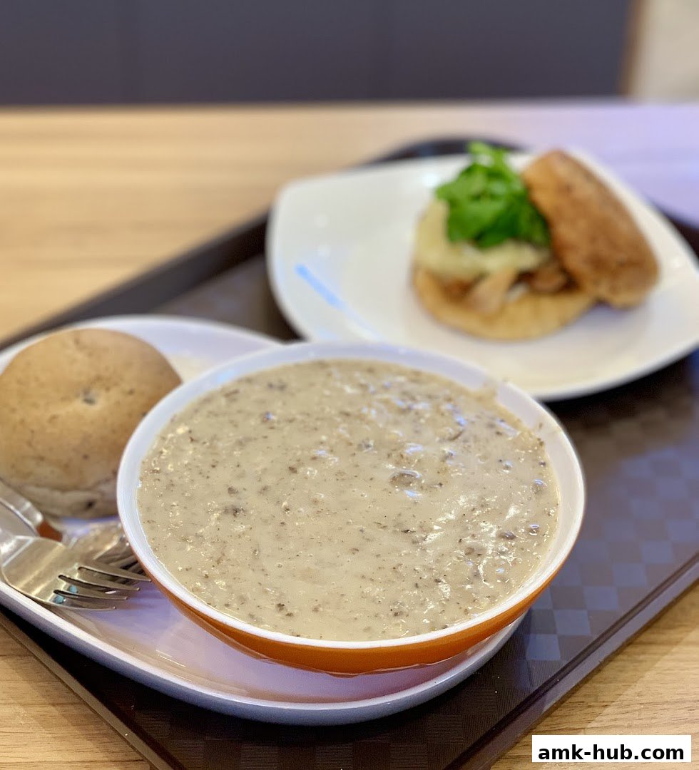 A bowl of creamy mushroom soup with a side bun and a mini sandwich.
