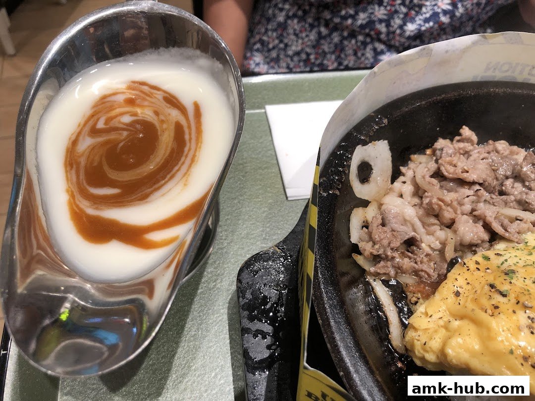A close-up of a sizzling hot plate meal with beef, onions, and a side of creamy sauce.