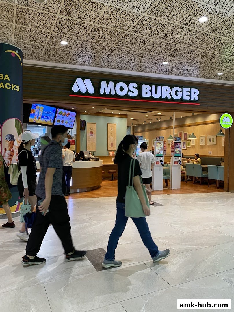People walk past the MOS Burger storefront in a mall, with the illuminated sign visible.