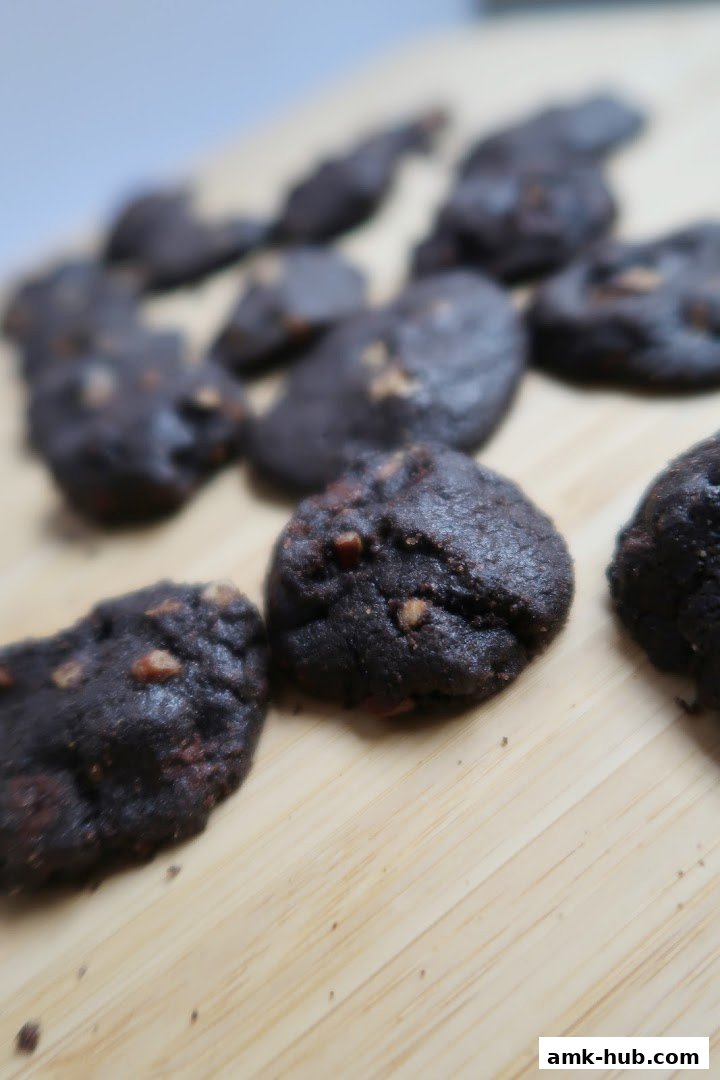 A close-up shot of several dark chocolate cookies with nuts on a wooden surface.