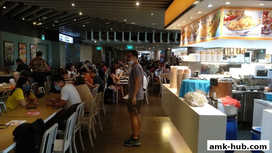 A busy food court with many people dining at tables and a serving counter.