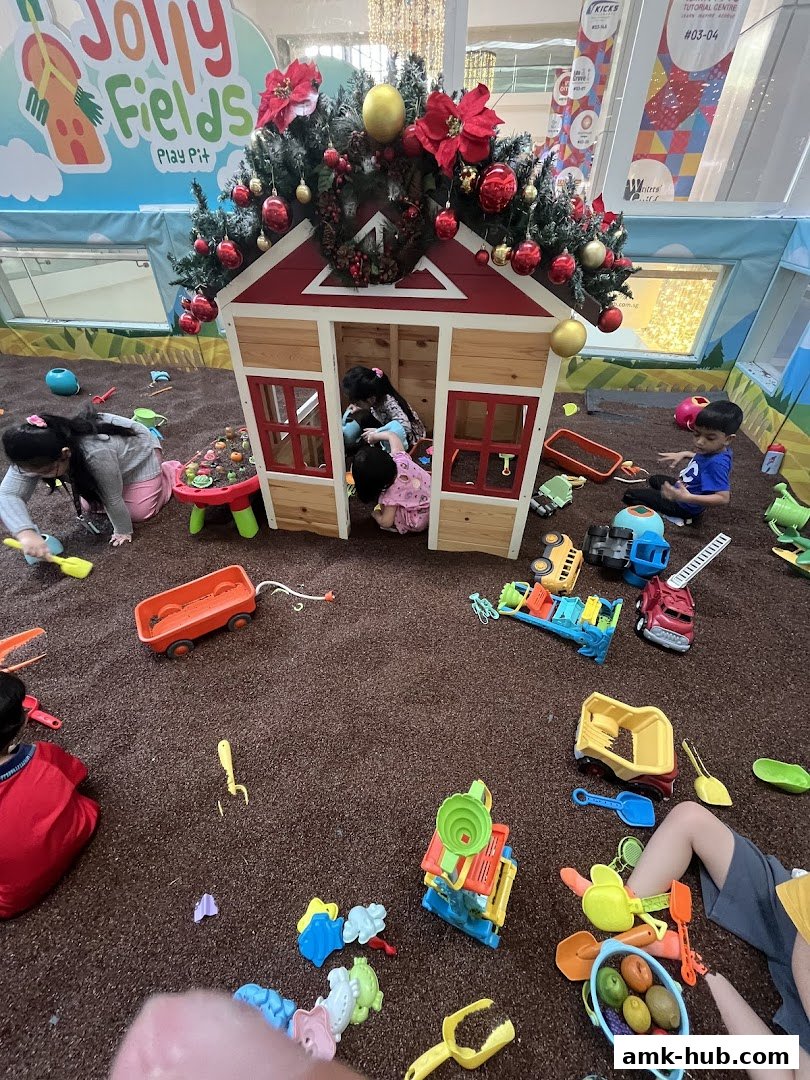 Children playing in a festive indoor sandpit with toys and a playhouse decorated for Christmas.